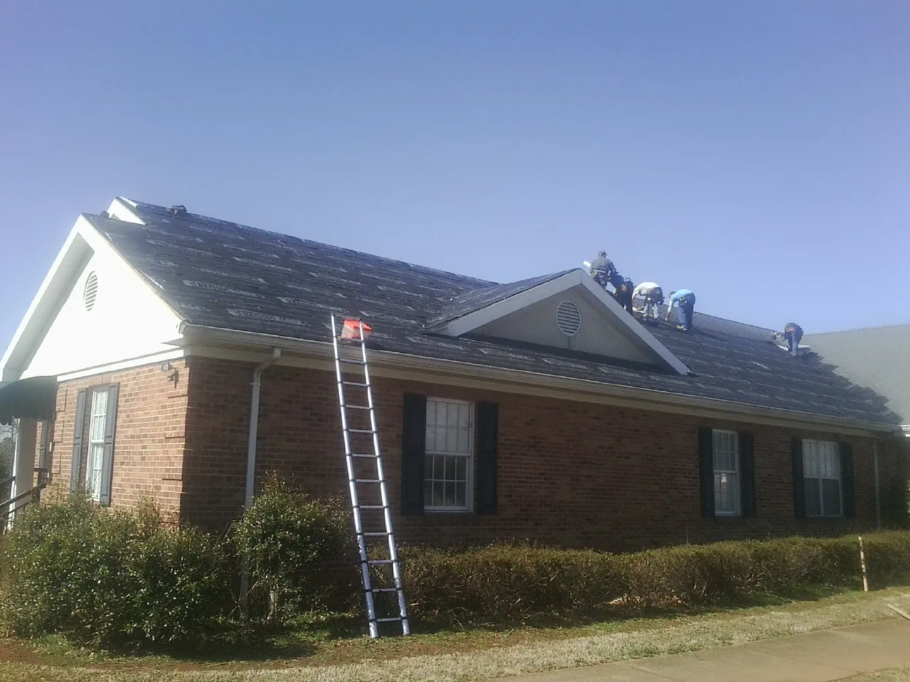Crew tearing shingles off a brick ranch roof with a ladder set — Metal Roof Repair work by our crew in Perryville
