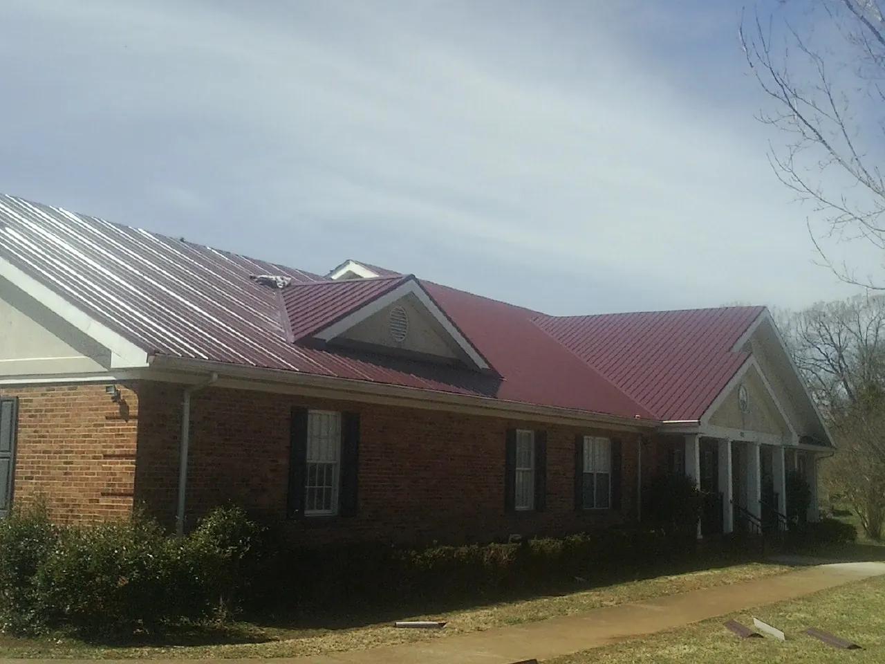 Red metal roof with gabled entries on a long brick building, from a Hail Damage Roof Repair job in Perryville