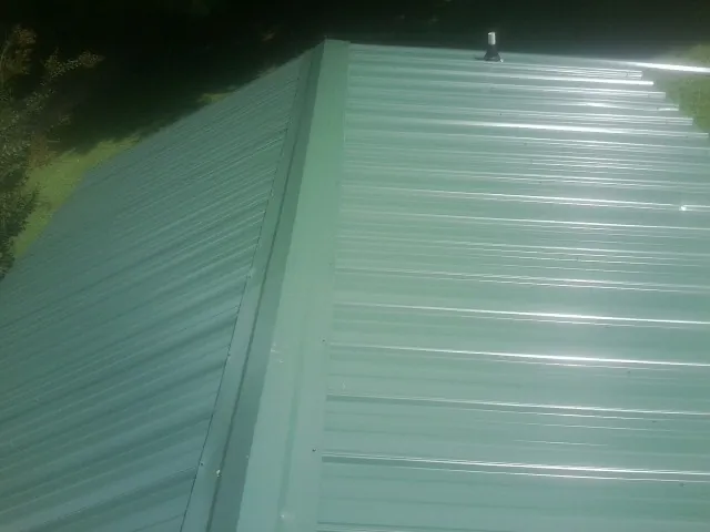 New green metal panels meeting at the ridge of a roof — Flat Roof Repair work by our crew in Perryville